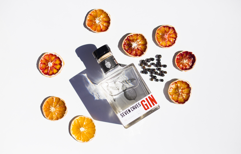 Bottle of Seven Caves Spirits Gin with dried oranges and juniper set around it.