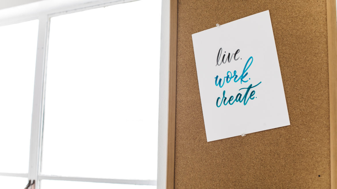 a sign reading "Live. Work. Create." pinned to a cork board.