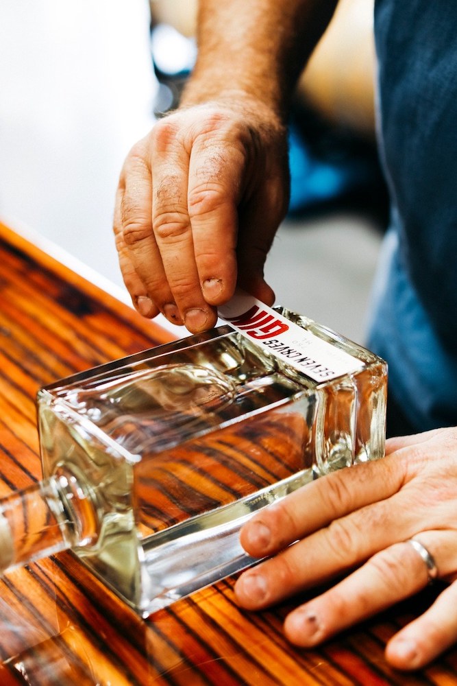 A label is being hand-placed on a bottle of Seven Caves gin