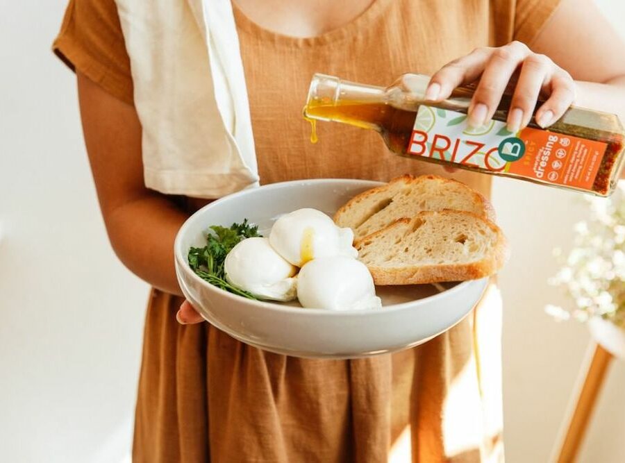 A woman pouring Brizo Everything Dressing on burrata cheese and bread.